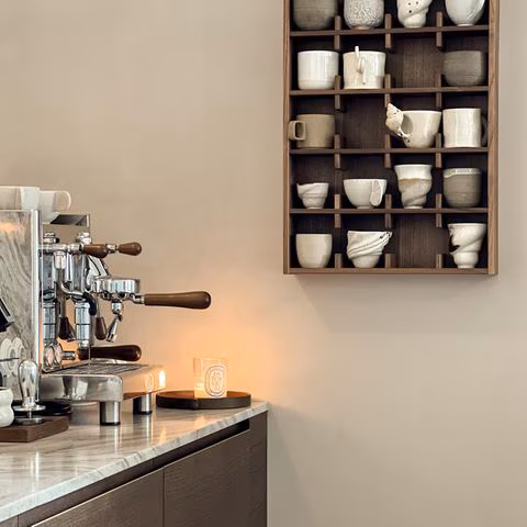 Tassenregal an der Wand mit Keramik, daneben eine Küchenzeile mit Siebträgermaschine und Marmorarbeitsplatte