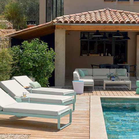 Drei Sonnenliegen mit dicken Polstern neben dem Pool auf mediterraner Terrasse