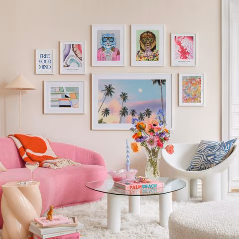 Wohnzimmer mit heller Wand, rosa Couch, bunten Bildern an der Wand und flauschigem weißen Teppich