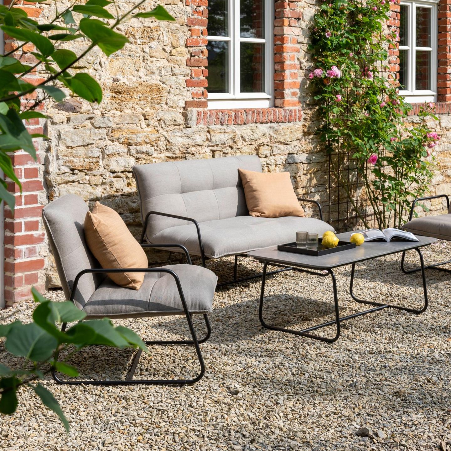 Outdoor Lounge mit schwarzem Metallrahmen und grauen Polstern vor einer rustikalen Backsteinwand