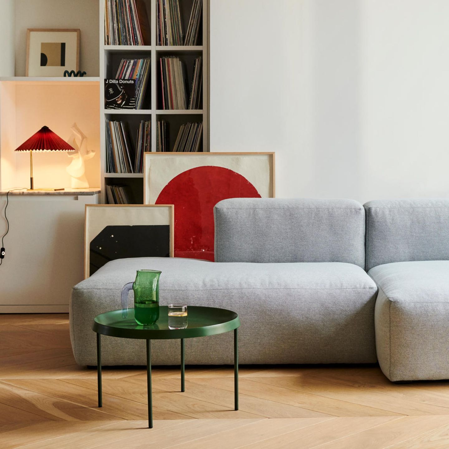 Wie gerne würden wir es uns in diesem Wohnzimmer bequem machen und uns duch die Plattensammlung hören: Neben dem grauen Polstersofa sorgen Accessoires wie Tischleuchte, Beistelltisch, Plaid und Blumenstrauß für tolle Farbakzente und bringen Lebendigkeit in den Raum. www.hay.dk